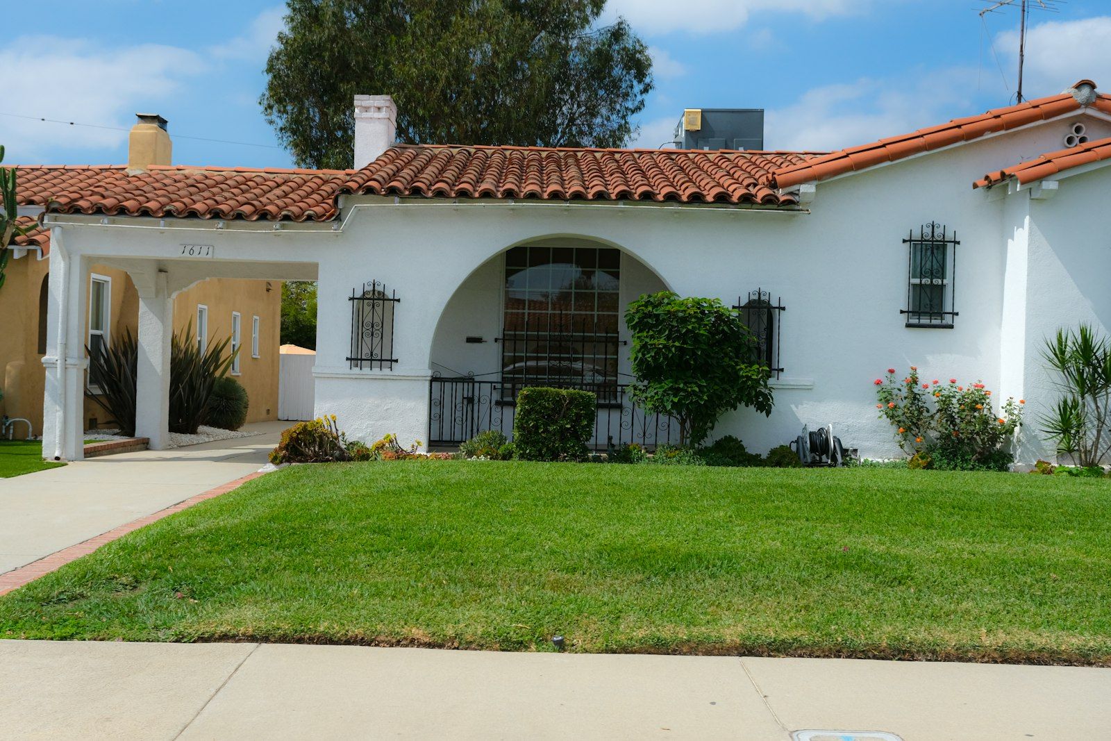 White stucco Spanish-style house with a red tile roof and a green front lawn