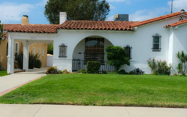 White stucco Spanish-style house with a red tile roof and a green front lawn